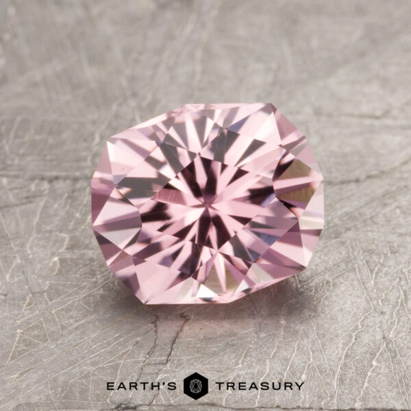 The ET1610, a pink gemstone with intricate facets, rests on a textured gray surface.