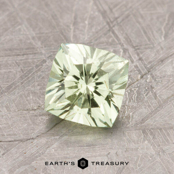 A 1.35-carat mint garnet, cut in a square shape and featuring a pale green hue, is displayed on a textured surface with the words "Earth's Treasury" visible beneath it.