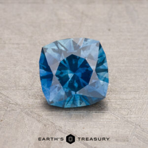 A 1.13-carat heated Montana sapphire with a cushion cut rests on a textured surface.