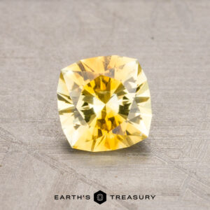 A 1.06-carat heated Montana sapphire with a faceted yellow hue rests on a textured surface.