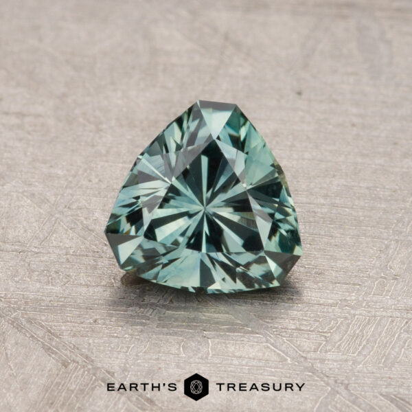 A trilliant-cut bluish-green gemstone, weighing 0.80 carats, elegantly displayed on a textured surface with the label "Earth's Treasury" below.