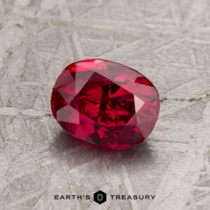 A 1.49-carat ruby rests on a metallic textured surface.