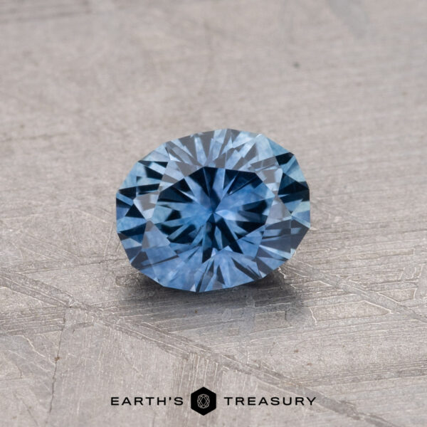 A round, faceted blue 0.81-carat Montana Sapphire (heated) placed on a textured gray surface, with the text "Earth's Treasury" at the bottom.