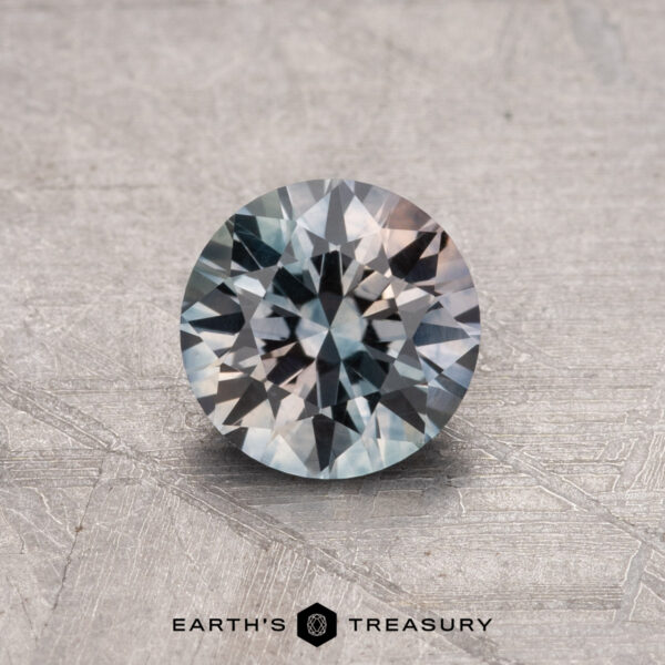 A round 1.14-carat Montana Sapphire (heated) with a faceted surface is placed on a textured gray background, and the text "Earth's Treasury" appears at the bottom.