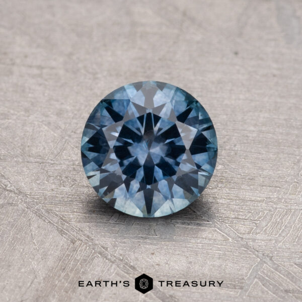 0.84-carat Montana sapphire, heated, rests on a textured surface with the "Earth's Treasury" logo at the bottom.