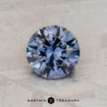 A round, blue 1.36-carat Montana sapphire with intricate facets is placed on a textured, light gray surface. The logo "Earth's Treasury" is visible below.