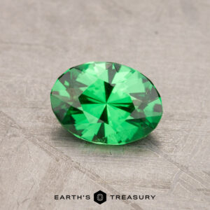 A 0.91-carat round, faceted tsavorite garnet on a textured surface with the "Earth's Treasury" logo at the bottom.