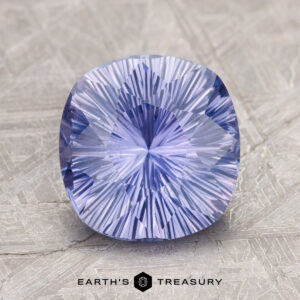 A cushion-cut, radiant blue-purple gemstone displayed on a textured surface, labeled as "2.60-Carat Ceylon Sapphire" by Earth's Treasury below it.