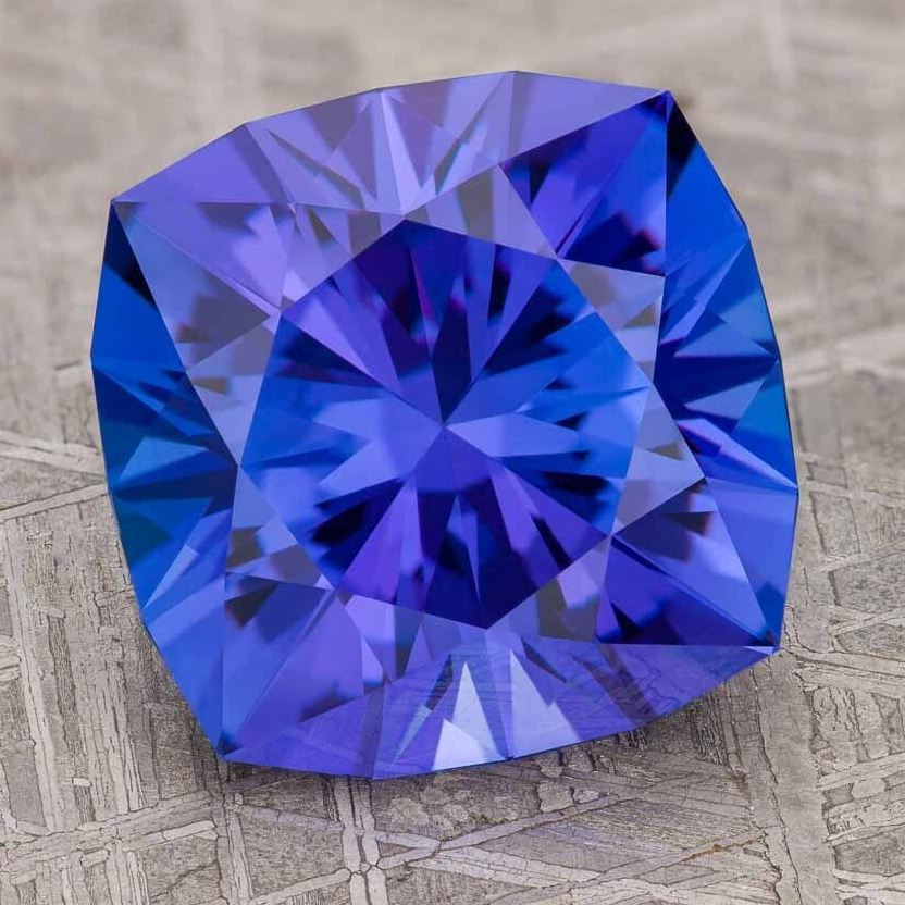 A heat-treatment-of-tanzanite gemstone with a faceted, blue-violet geometric cut rests on a textured metallic surface.